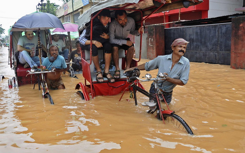 Rickshaw pullers wade through a flooded road after heavy rains at Guwahati